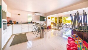 A modern kitchen with white cabinets, a dining area with a table and chairs, and a view of the outdoors. - Cottage Beach House NBBC 1 – Beachfront Escape, Just Steps from the Sea (Baie Nettlé)