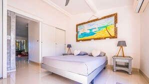 A bedroom with a large bed, a painting on the wall, and a small table with a lamp. - Cottage Beach House NBBC 1 – Beachfront Escape, Just Steps from the Sea (Baie Nettlé)