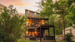 Une maison à plusieurs étages dotée d’un patio couvert, d’un espace salon extérieur et offrant une vue sur les arbres environnants.