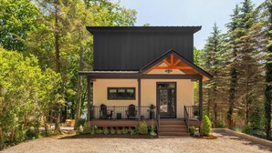 Een modern huis met twee verdiepingen en een overdekte veranda, omgeven door dicht bos.