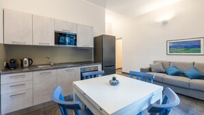 A compact kitchen with modern appliances, a dining area with blue chairs, and a living space with a sofa and a painting. - AMARI APARTMENT DOWNTOWN PALERMO (Palermo)