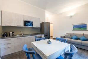 Una cucina compatta con elettrodomestici moderni, un tavolo da pranzo con sedie e un divano in un soggiorno con un quadro appeso al muro.