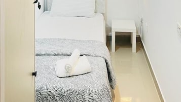 Ein Schlafzimmer mit einem Bett, einem Nachttisch, einer Wanduhr, einer kleinen Ablage mit einer Pflanze und einer Wand mit gerahmten Bildern.