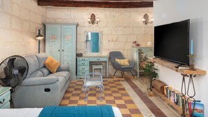 Ein gemütliches Zimmer mit kariertem Boden, einem Sofa, einem Schaukelstuhl, einem Fernseher und einem Bücherregal.