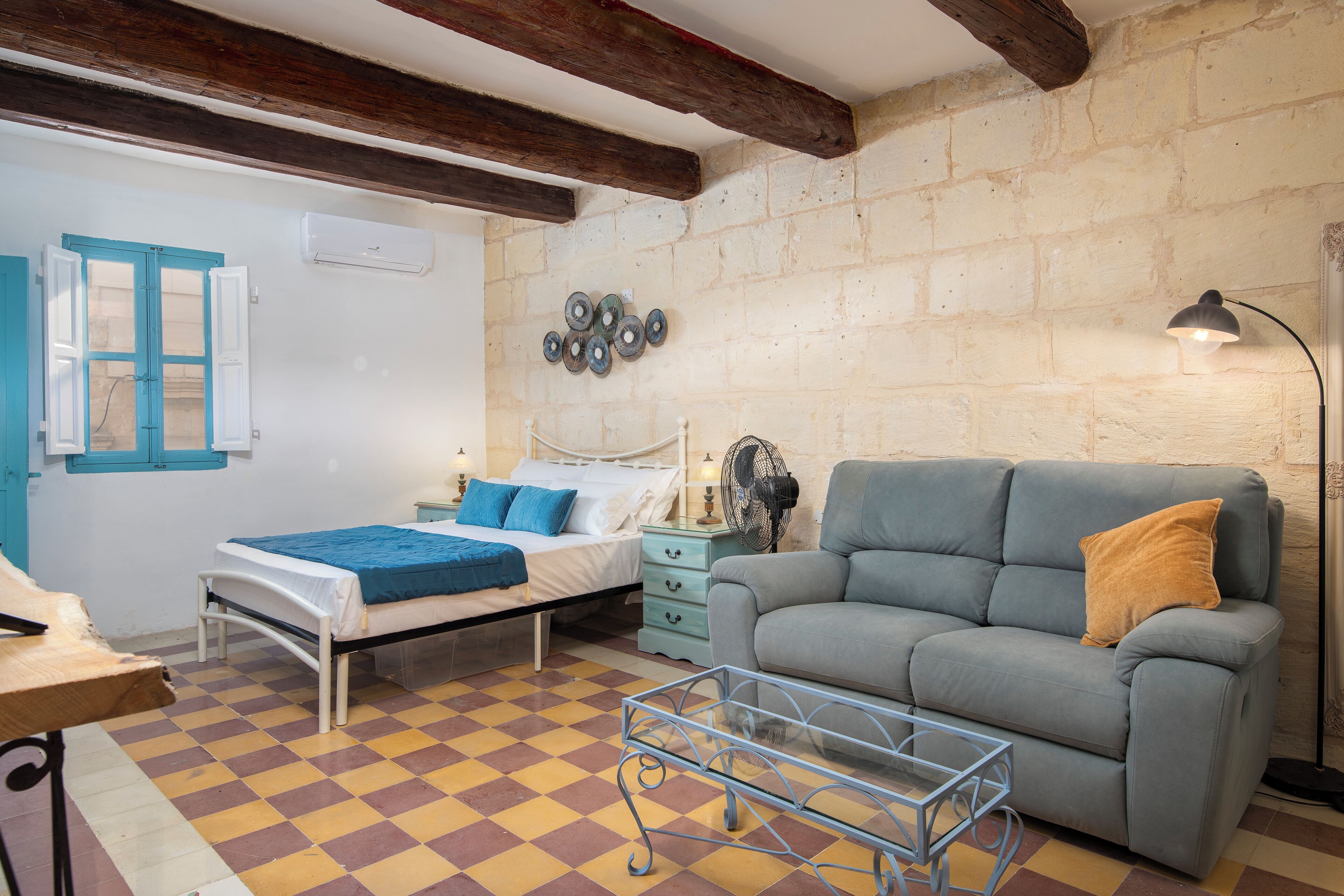 A room with a bed, a sofa, a small table, and a fan.
