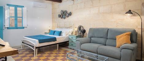 A room with a bed, a sofa, a small table, and a fan.