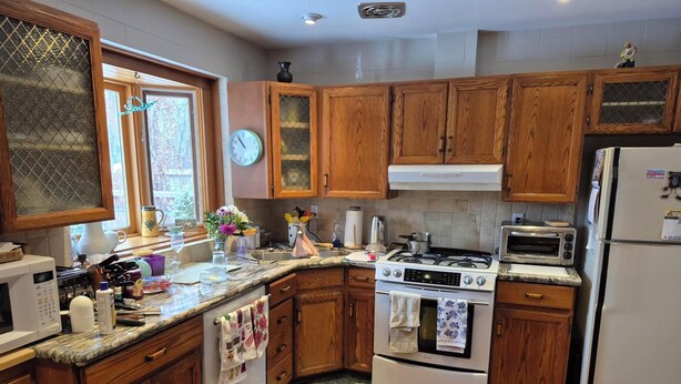 A kitchen with wooden cabinets, a stove, a microwave, and a refrigerator. - Charming 3-bedroom bungalow in peaceful Vaughan with AC and heat. (Vaughan)