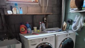 A laundry area with two front-loading washing machines, a small sink, and various cleaning supplies on a shelf. - Charming 3-bedroom bungalow in peaceful Vaughan with AC and heat. (Vaughan)