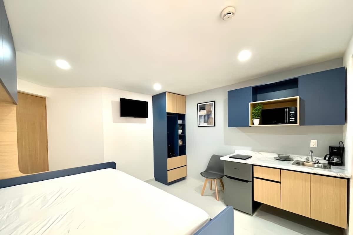 Une chambre d’hôtel de taille réduite, comprenant un lit, un bureau, une chaise, un four à micro-ondes, un lavabo et un petit placard.