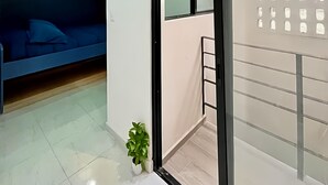 A modern apartment with a blue sofa, a small potted plant, and a sliding glass door leading to a balcony. - Living Alameda (Queretaro)