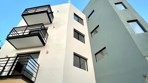 A modern multi-story building with balconies and a large garage door. - Living Alameda (Queretaro)