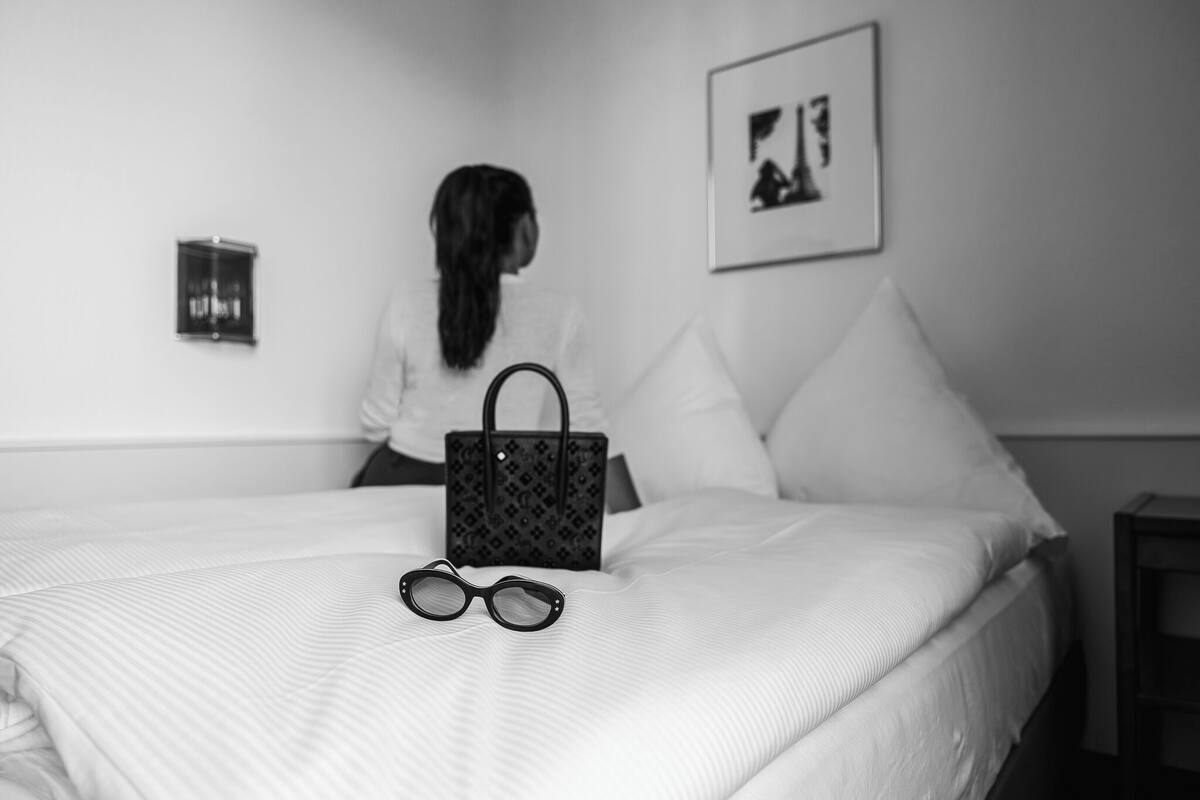 A bed with a striped bedspread, a pair of glasses, and a handbag on it.