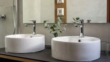 Two round white sinks with chrome faucets, a mirror above, and a small plant on the counter.