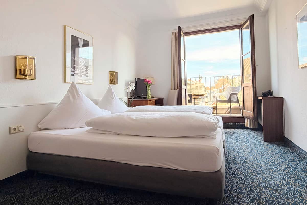 A hotel room with a bed, a TV, a desk with a lamp, a chair, and a balcony with a view.