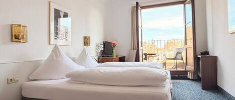 A hotel room with a bed, a TV, a desk with a lamp, a chair, and a balcony with a view.