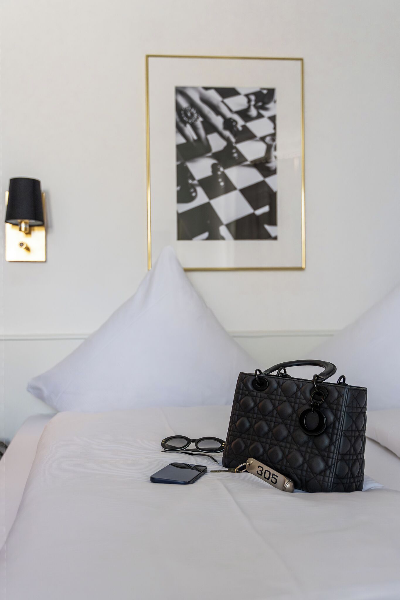 A neatly made bed with a black quilted handbag, a pair of glasses, and a keychain with the number 305 on it.