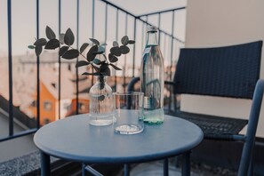 A round table with a glass bottle, a glass, and a vase with leaves on a balcony. - Hotel Boulevard (Konstanz)
