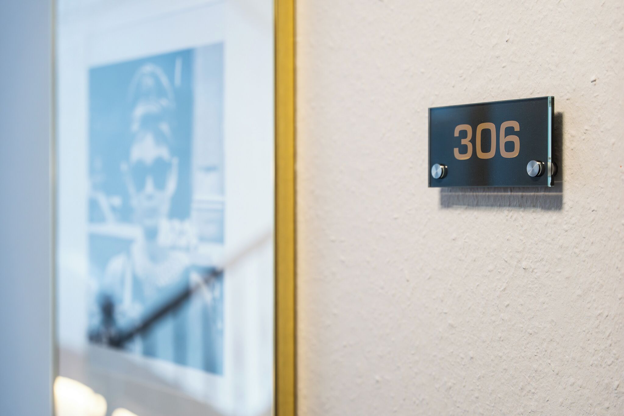 A wall-mounted number plate with the number 306, a door frame, and a partial view of a poster.