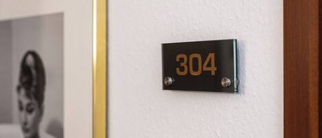 Musta metallilaatta, jossa on numero ’304’, on kiinnitetty valkoiseen seinään.