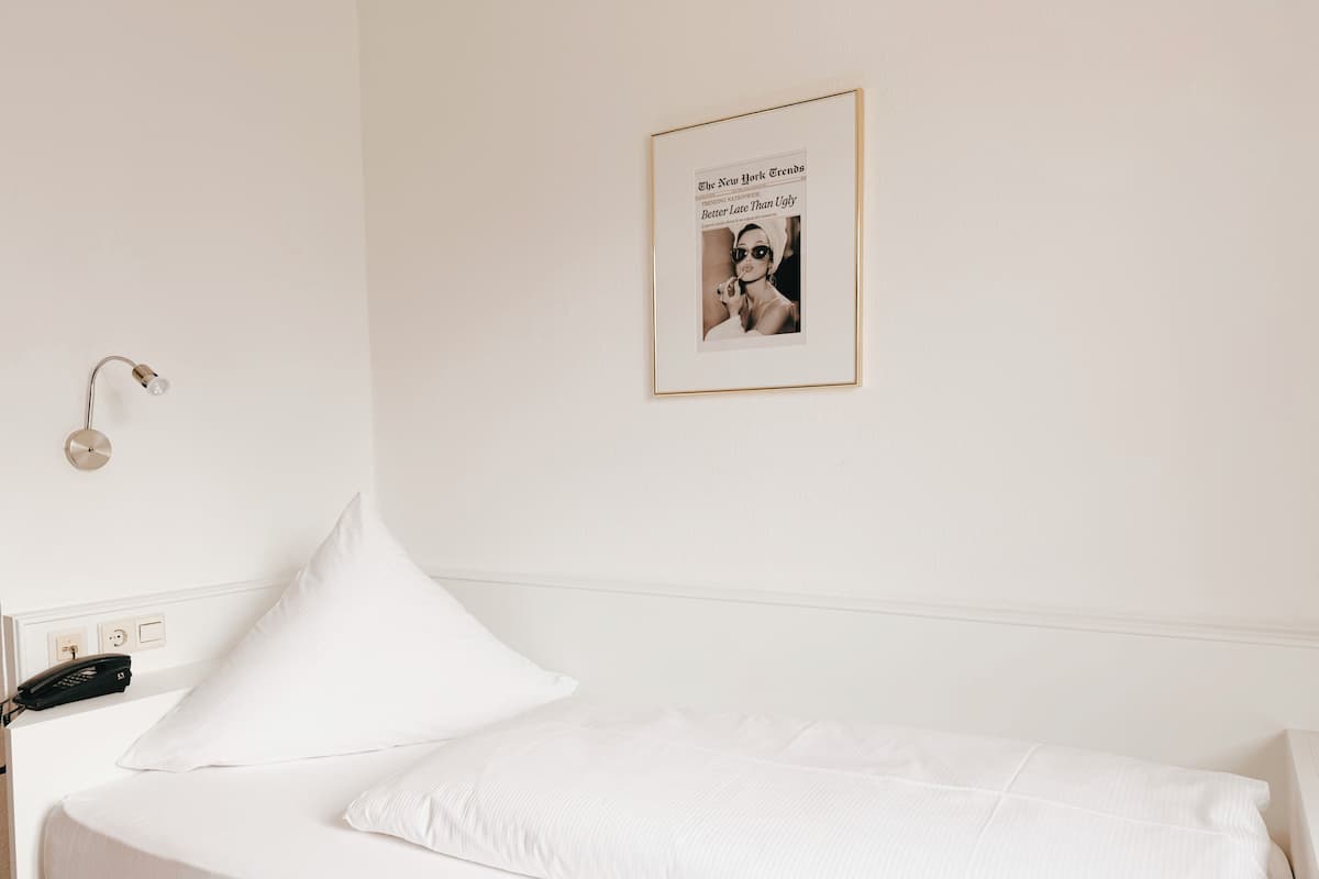 A single bed with white bedding, a wall-mounted light fixture, and a framed picture on the wall.