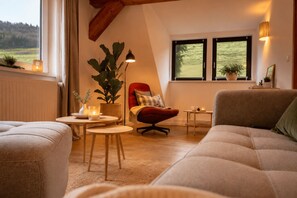 A cozy living room with a red armchair, a grey sofa, a small table with candles, and a large plant. - Harz Vacation Rental I Balcony & Mountain View (Osterode am Harz)
