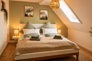 A bedroom with a bed, two wall-mounted lamps, a window, and two framed pictures. - Harz Vacation Rental I Balcony & Mountain View (Osterode am Harz)