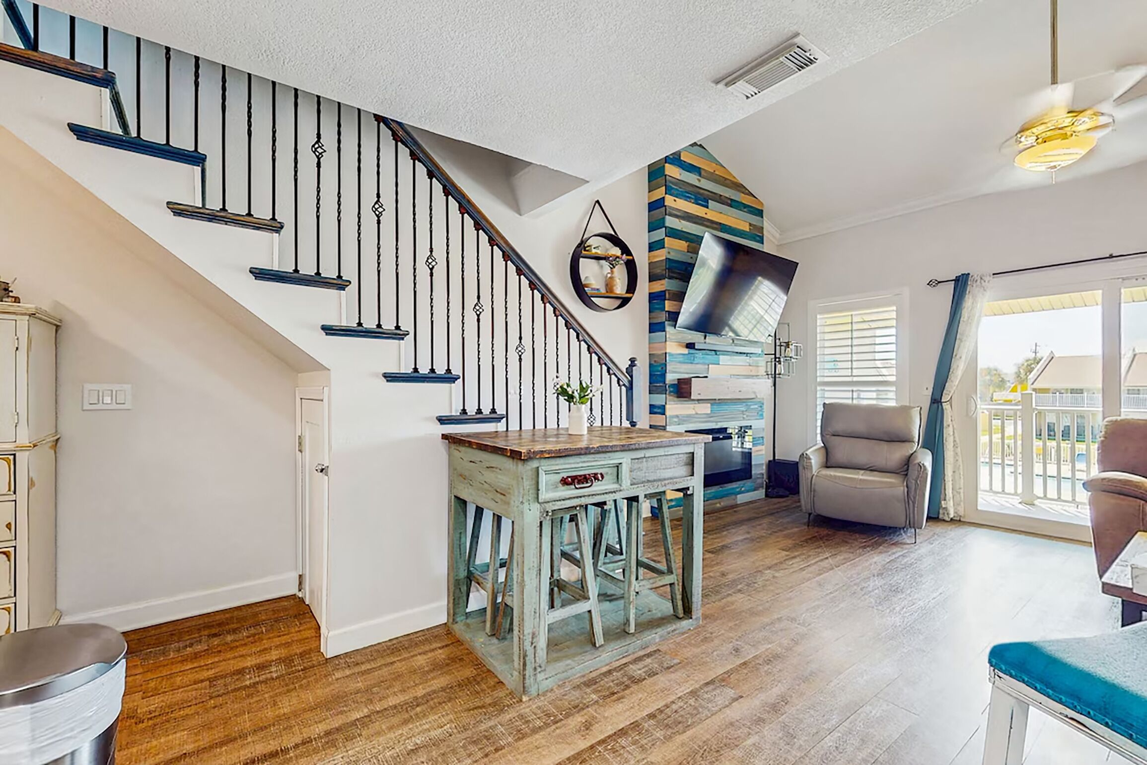 A staircase with black balusters, a wooden table with a vase, and a modern ceiling fan.