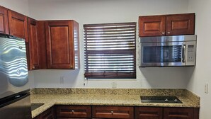 A kitchen with wooden cabinets, a stainless steel refrigerator, a microwave, and a window with blinds. - 110 Signature Single Room in waterfront hotel in Singer Island, FL (Riviera Beach)