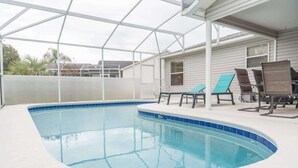 Une piscine intérieure à bords incurvés, entourée d’un patio couvert aménagé avec des chaises longues et offrant une vue sur un immeuble d’habitation en arrière-plan.