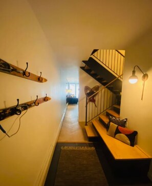 A narrow hallway with a wooden bench, a staircase with a metal railing, and wall-mounted coat hooks.