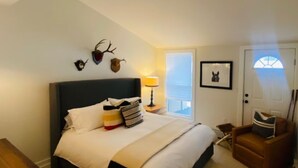 Ein Schlafzimmer mit Bett, Nachttisch mit Lampe, Stuhl, Tür mit Fenster und Wanddekorationen.
