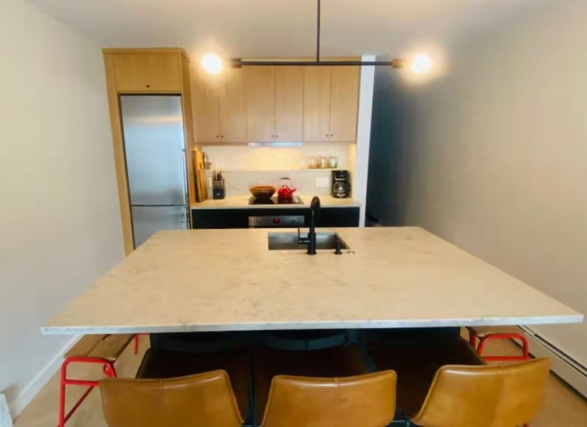 A compact kitchen with a central island, wooden cabinets, and a stainless steel refrigerator.