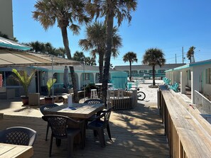 A wooden deck with outdoor seating, palm trees, and a building with teal accents. - Sea Vista Resort And Tiki Bar (New Smyrna Beach)