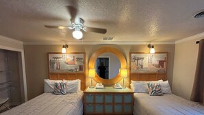 Ein Hotelzimmer mit zwei Betten, einem Deckenventilator, einem runden Spiegel und Bildern an den Wänden.