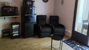 Un espace de vie compact comprenant un réfrigérateur noir, un four à micro-ondes, une petite table, deux chaises noires et un plancher en bois.