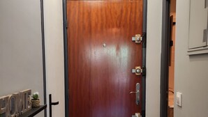 Un couloir avec une porte en bois, une étagère ornée d’objets décoratifs et un interrupteur sur le mur.