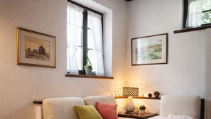 Un salon chaleureux avec un canapé d’angle, une petite table d’appoint, un tapis et deux tableaux encadrés accrochés aux murs.