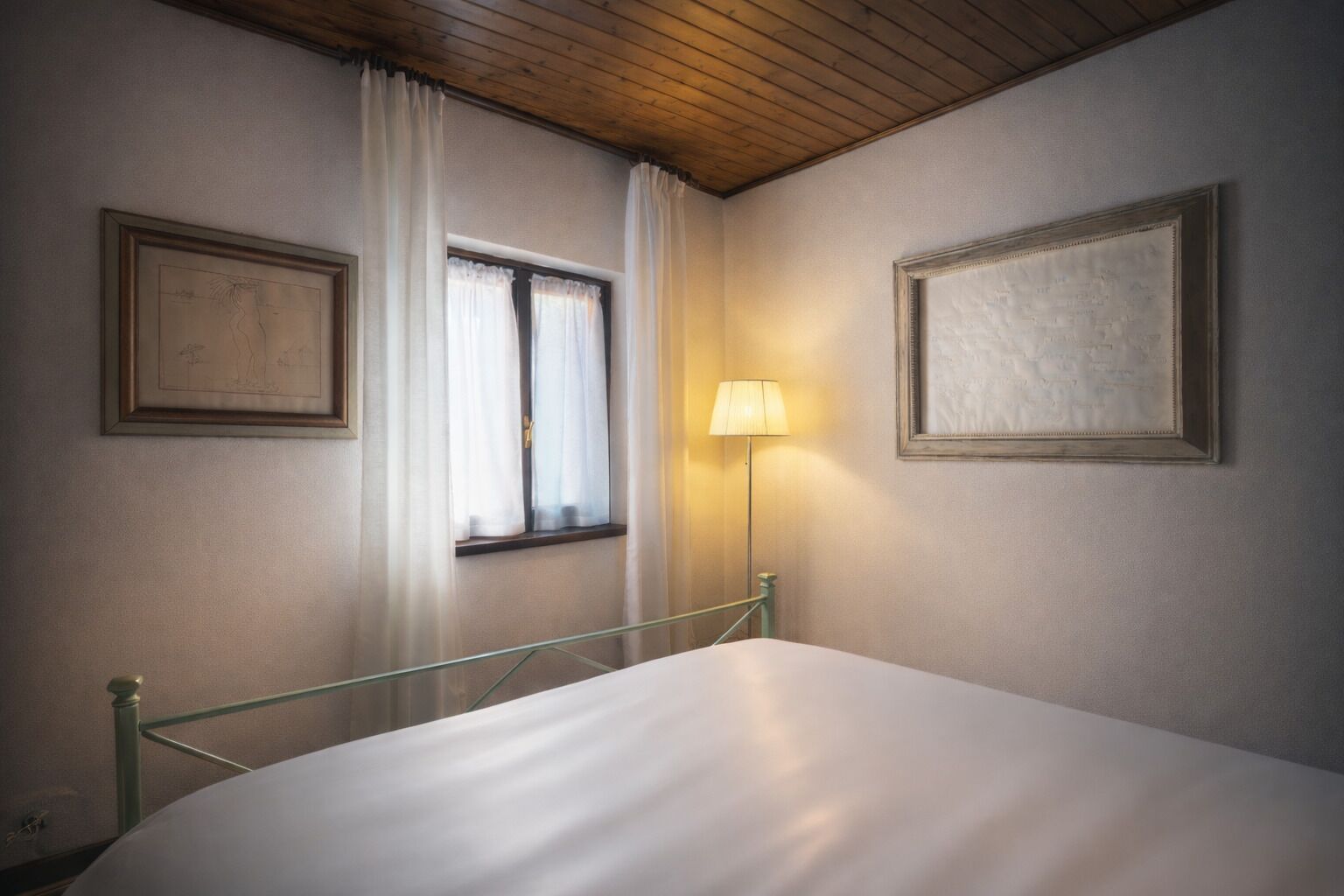 A bedroom with a bed, a window with curtains, and two framed pictures on the wall.
