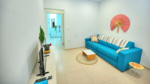 A modern living room with a blue sofa, a small wooden coffee table, a TV stand, and a decorative fan on the wall. - Seafront Sea View Maisonette with Yards (St. Paul's Bay)