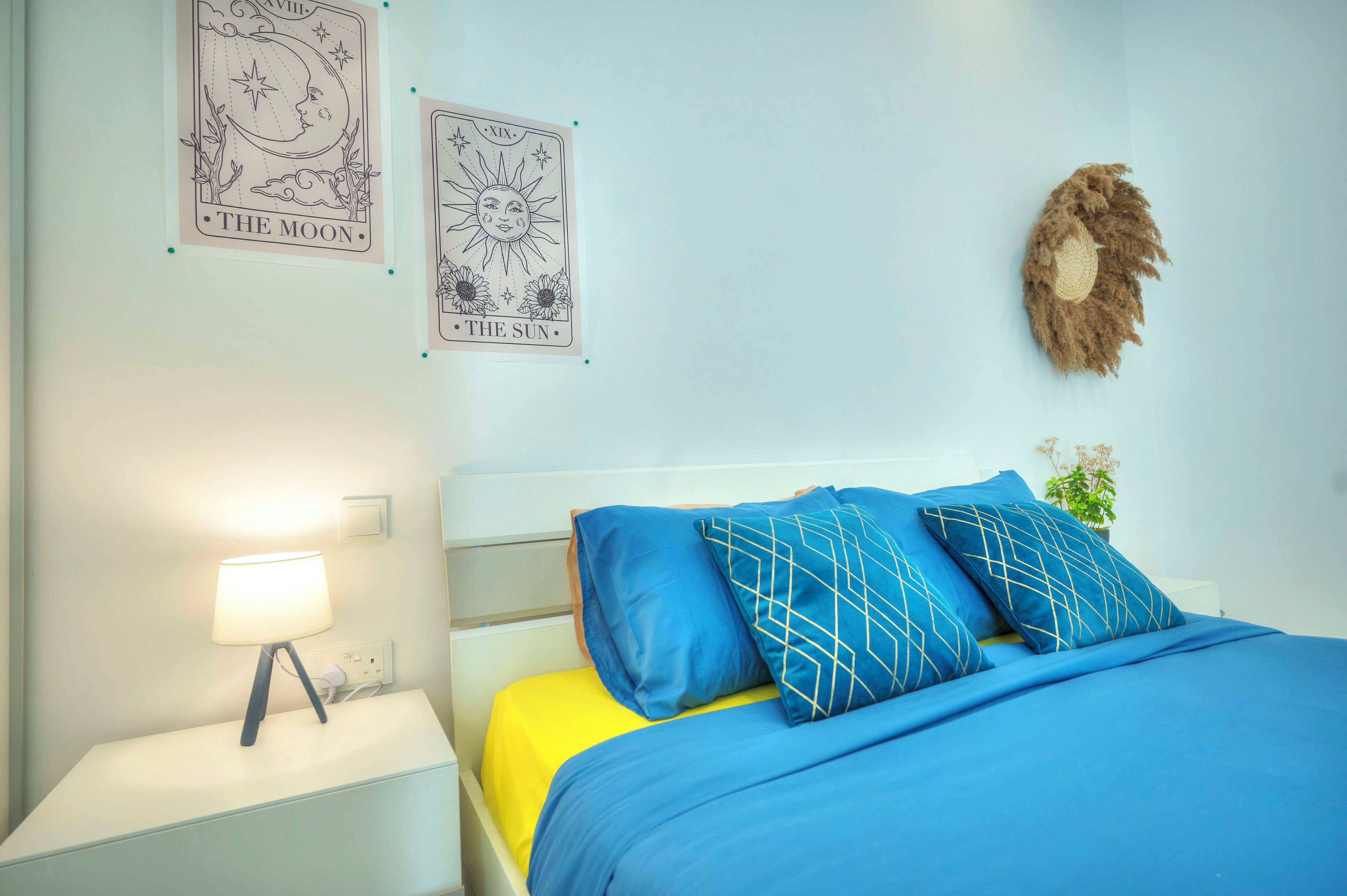 Un dormitorio con cama, mesita de noche, lámpara y dos adornos en la pared que dicen "The Moon" y "The Sun".