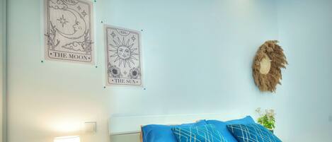 Un dormitorio con cama, mesita de noche, lámpara y dos adornos en la pared que dicen "The Moon" y "The Sun".