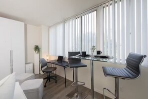 A modern, well-lit room with a glass table, two chairs, a laptop, and a small plant. - Beach-Close Santa Monica - Prime Location (Santa Monica)