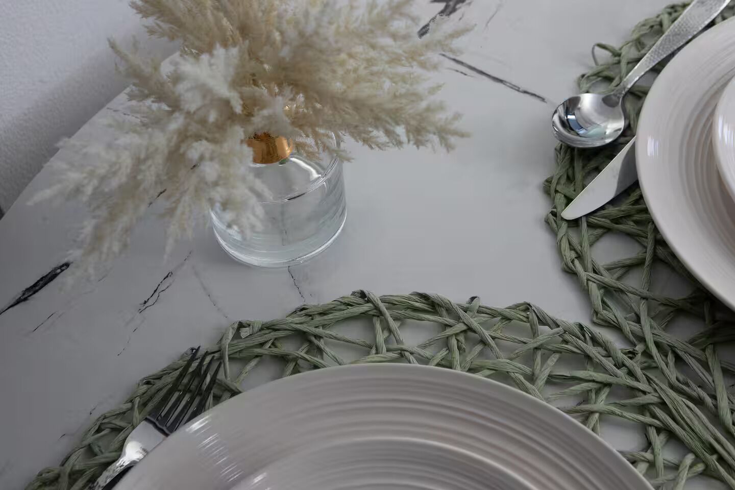 Une table dressée avec de l’argenterie, des assiettes blanches et un vase en verre transparent contenant des fleurs blanches.