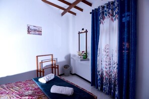 Ein Schlafzimmer mit Bett, Stuhl, einem kleinen Tisch mit einer Vase und einem Spiegel an der Wand.