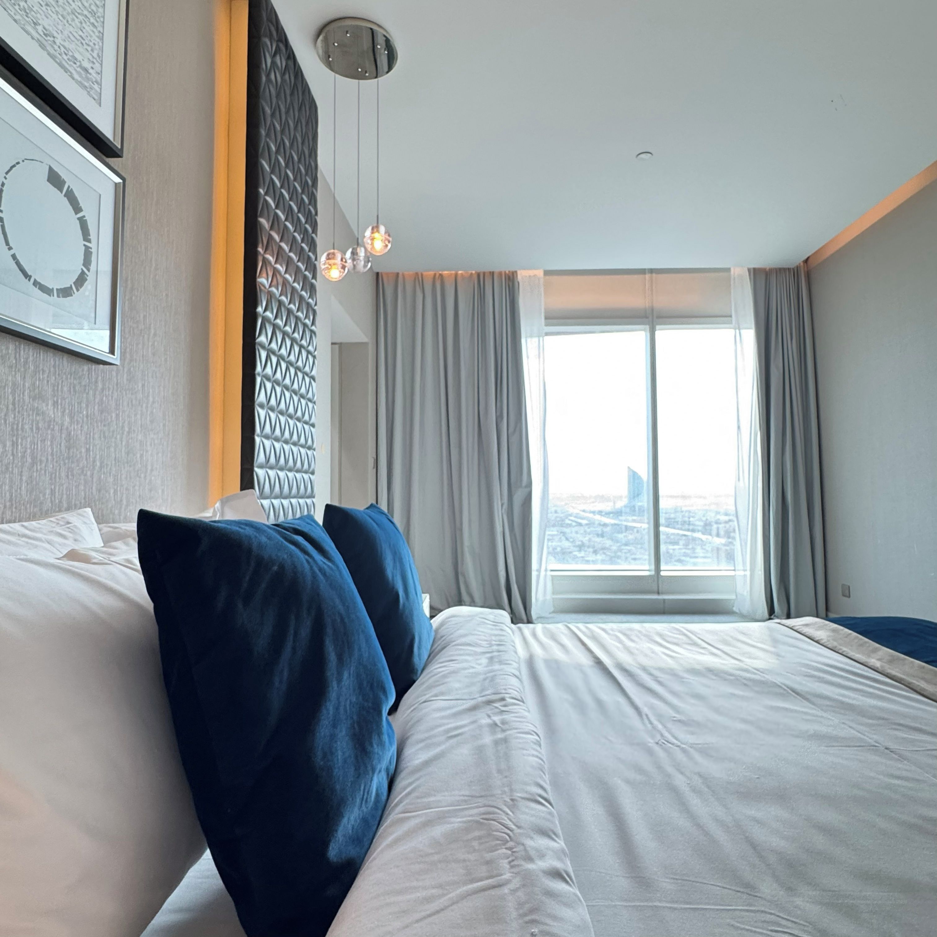 Une chambre d’hôtel avec un grand lit, une vue sur la ville et un luminaire moderne.