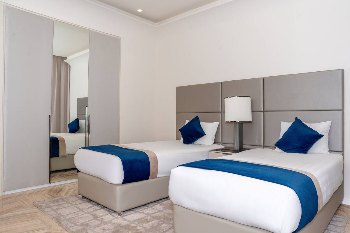 A hotel room with two beds, a mirror, a nightstand, and a lamp.