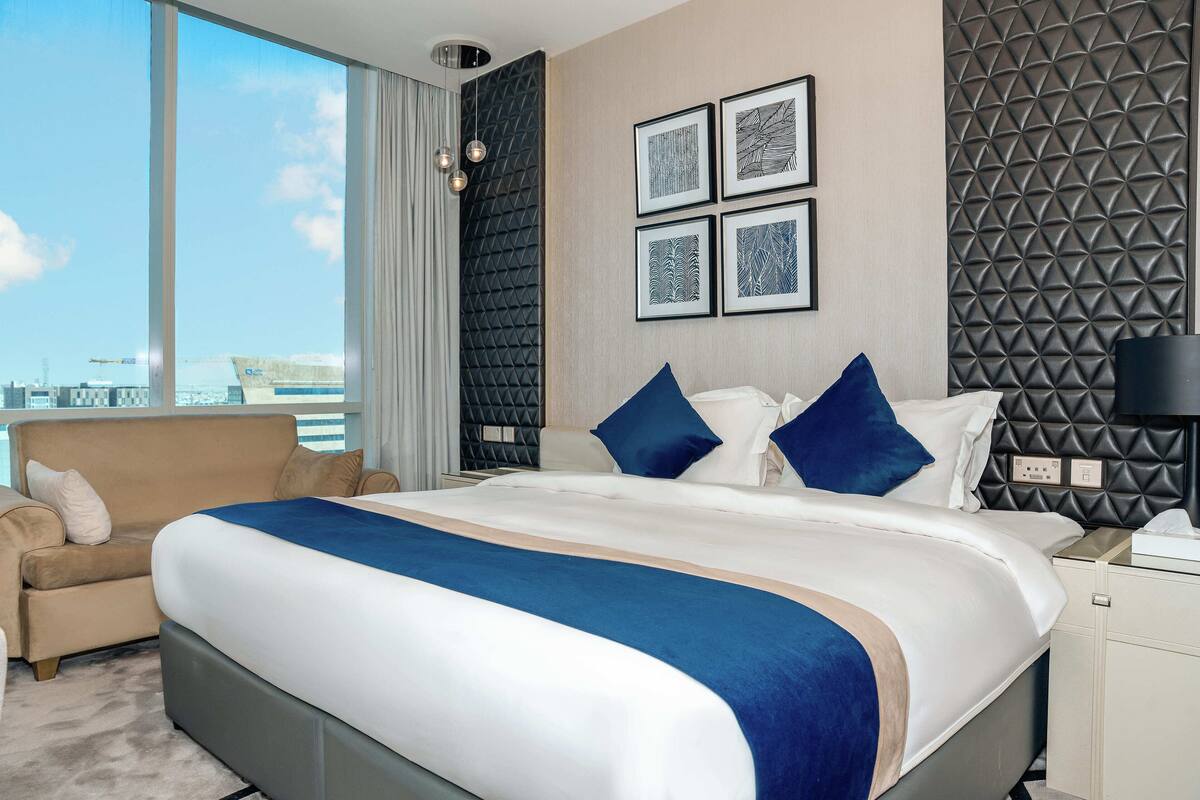 A modern hotel room with a large bed, a sofa, and a city view.