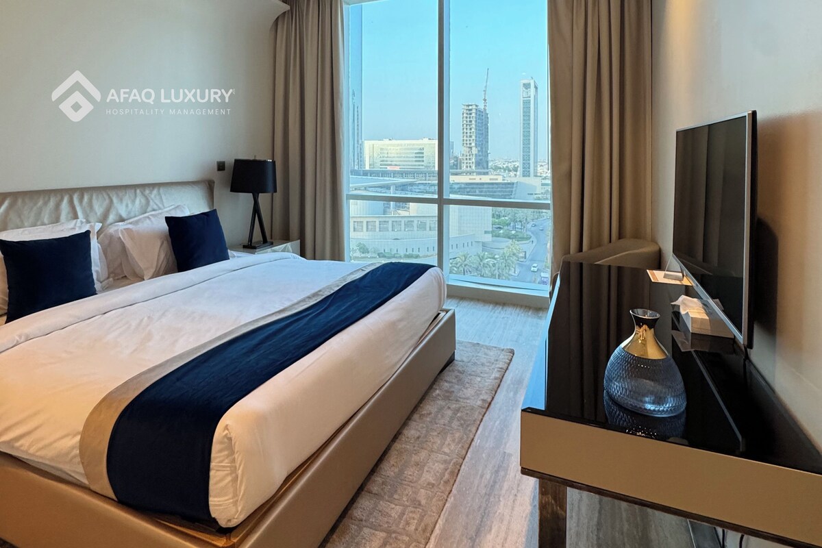 A hotel room with a large bed, a TV, a desk, and a view of the cityscape.