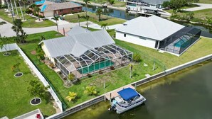 An aerial view of a residential area with a large house featuring a glass-enclosed patio and a swimming pool. - Cape Coral Waterfront Retreat - Pool, Spa & Tropical Tommy Bahama Style - Pets (Cape Coral)