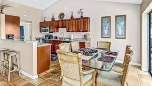 Un'ampia cucina con mobili in legno, un'isola centrale e un'area pranzo con sedie in vimini e un tavolo in vetro.